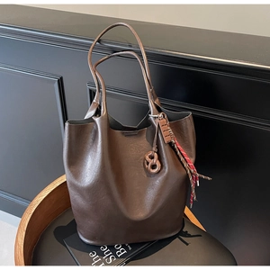 Détail du sac seau en cuir marron foncé avec breloque bretzel et pompon tissé