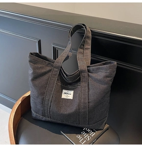 Detailed view of dark grey denim tote bag with external pocket on black leather background