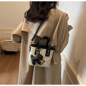 Détail du sac seau en toile avec garniture en cuir et breloque chiot sur l'épaule