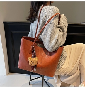 Brown vintage leather tote bag with plush bear charm worn by model in cozy sweater