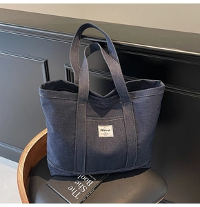 Detail of deep blue denim tote bag featuring a front pocket on a black leather chair