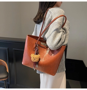 Detailed view of a brown leather tote bag featuring a cute plush bear charm accessory