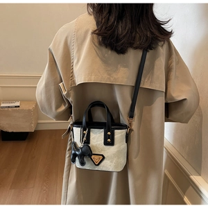 Détail du mini sac cabas crème avec bordure noire et charm de chien en cuir sur bandoulière