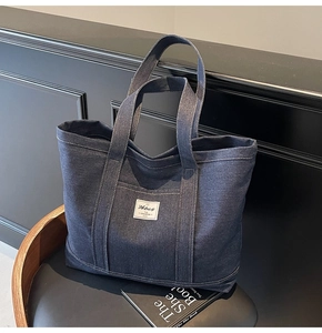 Detailed view of dark blue denim tote bag with contrast stitching and branded label