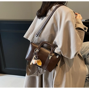 Sac à main marron avec breloques de baseball porté sur un trench-coat kaki classique