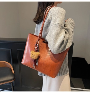 Detail of large brown leather tote bag with lychee texture and cute bear pendant