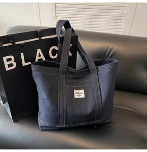 Detail of dark blue denim tote bag with industrial style brand label on black sofa