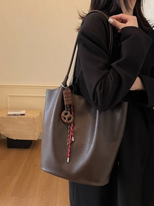 Sac cabas marron foncé avec breloque chocolat porté par un mannequin en décor épuré