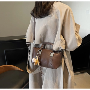 Détail du sac à main en cuir mat marron foncé avec breloque baseball et sangle