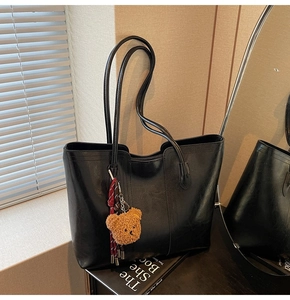Detail of black PU leather tote bag with vertical stitching and brown bear charm