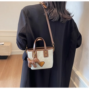 Détail d'un sac seau en toile beige avec garniture en cuir brun et breloque chiot