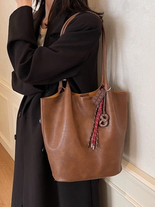 Sac seau vintage en cuir marron avec pendentifs porté par un mannequin dans un style épuré