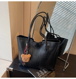Detail of black glossy tote bag with long straps and brown plush bear charm