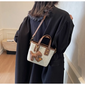 Détail du sac seau gris avec finitions en cuir marron, rivets et charmant pendentif chien