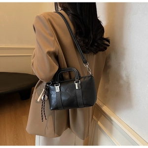 Détail d'un sac à main noir en cuir avec surpiqûres blanches et charme de boule