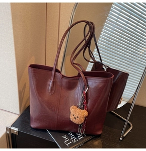 Detail of burgundy tote bag with glossy finish and cute plush bear charm on its handle