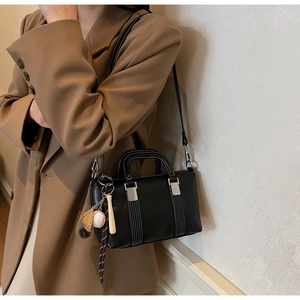 Détail du sac à main en cuir noir avec surpiqûres blanches et breloques de baseball