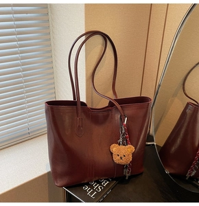 Close-up of deep red leather tote bag with soft teddy bear charm and large capacity