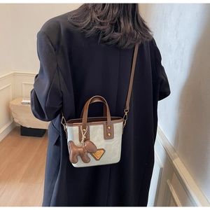 Détail du sac seau en toile grise avec garniture en cuir marron et breloque chiot mignonne