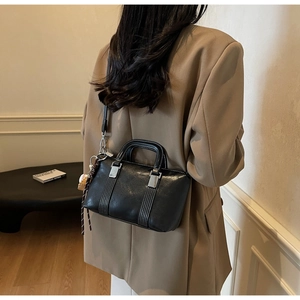Détail d'un sac à main noir avec coutures contrastées blanches et pendentif de baseball