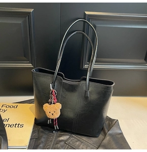Detail of a black leather tote bag featuring a cute brown plush bear charm accessory