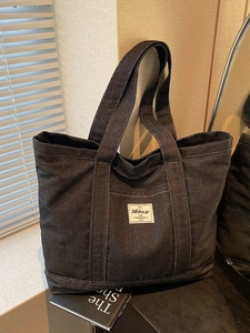 Large dark denim tote bag for women with dual handles and white label in a stylish setting