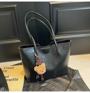 Detail of black faux leather tote bag featuring a cute plush bear charm and vertical seams
