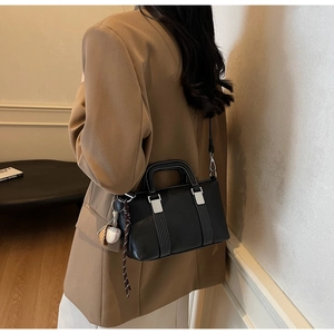 Détail du sac en cuir noir avec pendentif baseball et rivets sur un blazer marron