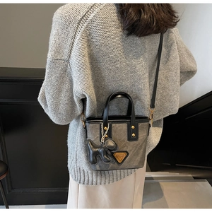Détail du sac seau gris texturé avec logo doré et charm de sac chiot noir élégant
