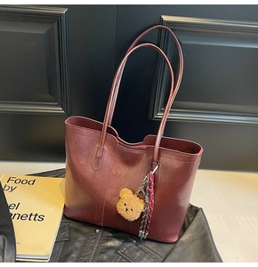 Detailed view of burgundy tote bag with plush bear charm on a black leather jacket
