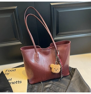 Close-up of deep red tote bag with vertical stitching and cute plush bear charm detail