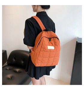 Detailed view of an orange quilted backpack featuring a textured honeycomb pattern and soft straps