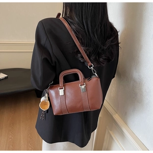 Sac bandoulière rétro marron avec surpiqûres et breloque baseball porté par un modèle