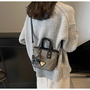 Détail du sac seau gris avec logo triangle doré et breloque chiot noir élégante