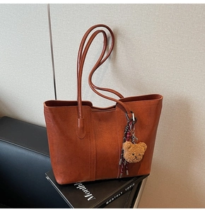 Detail of vintage caramel tote bag with plush bear charm and woven cord on a magazine