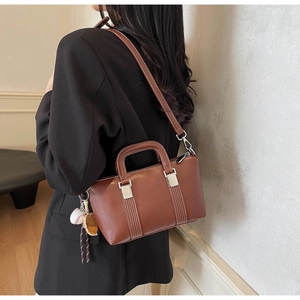 Vue détaillée du sac à main en cuir marron avec surpiqûres et pendentif baseball