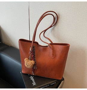 Detail of vintage brown tote bag with slim straps and cute plush bear keychain
