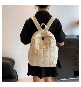 Detail of beige quilted backpack texture on model's back with adjustable straps