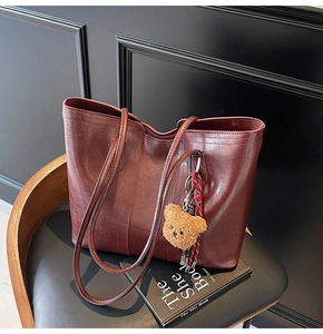 Close-up of vintage burgundy tote bag with plush bear charm on a black leather chair