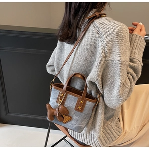 Détail du sac seau en denim bleu clair avec garniture en cuir brun et breloque chiot