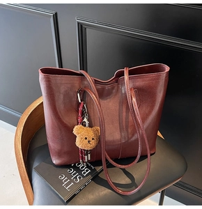 Close-up of vintage burgundy leather tote bag with plush bear charm on a classic chair