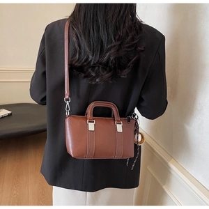 Détail du sac Boston en cuir marron avec surpiqûres blanches et charme de baseball