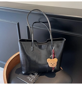 Detail of black faux leather tote bag with glossy texture and a cute brown plush bear charm