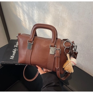 Détail du sac Boston marron foncé avec surpiqûres blanches et breloque de baseball