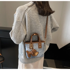 Détail du sac seau en denim bleu avec garniture en cuir brun et pendentif chien