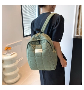 Seitenansicht eines salbeigrünen gesteppten Rucksacks an einem Model in moderner Umgebung
