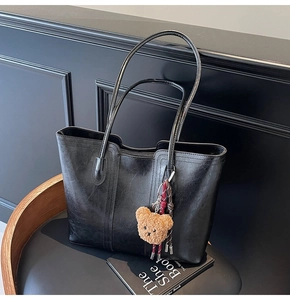 Detail of black leather tote bag with plush bear charm and sleek texture on black leather chair