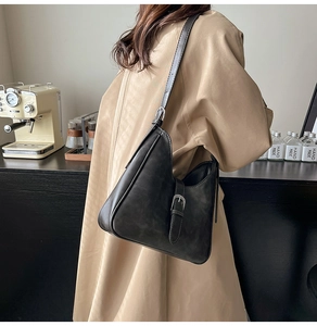 Gros plan d'un sac bandoulière vintage en cuir noir avec boucle argentée sur un trench-coat