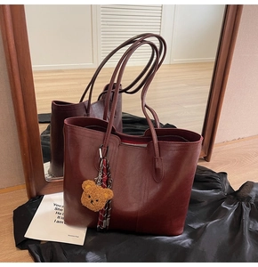 Detail of burgundy large tote bag with shiny leather texture and brown teddy bear charm
