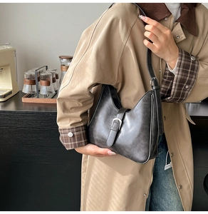 Détail d'un sac hobo rétro gris foncé porté avec un trench-coat classique élégant